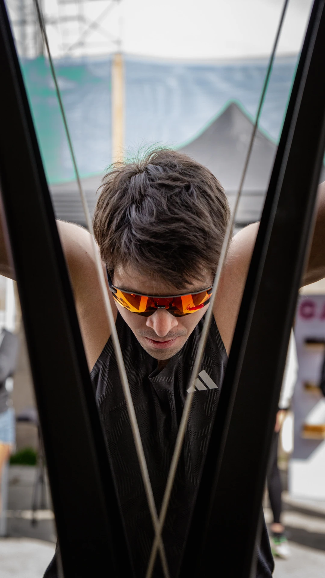 Primer plano de un atleta con gafas de sol naranjas en la estación de SkiErg de Hybrid Monkey V3, enmarcado por los cables y la estructura de la máquina.